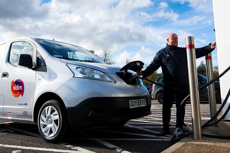 A Mitie branded electric van being charged, 一名Mitie员工在货车前面操作充电点系统